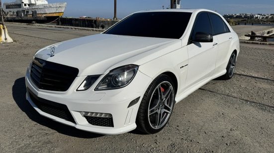 A white Mercedes-Benz E63 AMG sedan in gloss white with silver alloy wheels, photographed against the waterfront