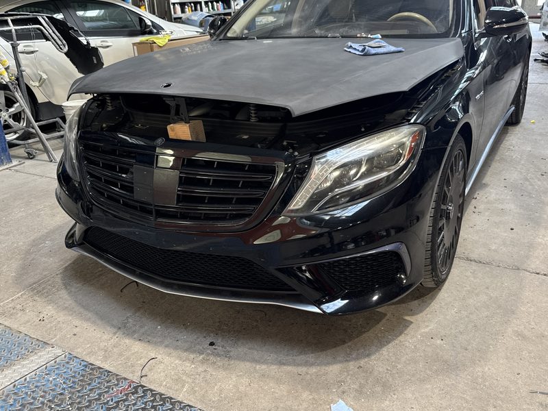 A black Mercedes-Benz S-Class inside the workshop with its hood removed and the front end stripped back to the bumper reinforcement.