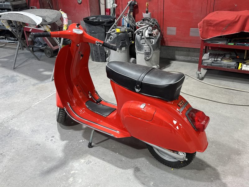 A Vespa scooter in bright red gloss standing on the workshop floor in front of a red tool cabinet.