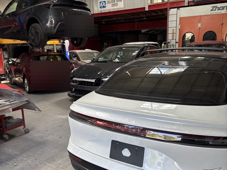 The workshop interior: a vehicle raised on a two-post lift, cars lined up along the bay and the paint booth at the far end.